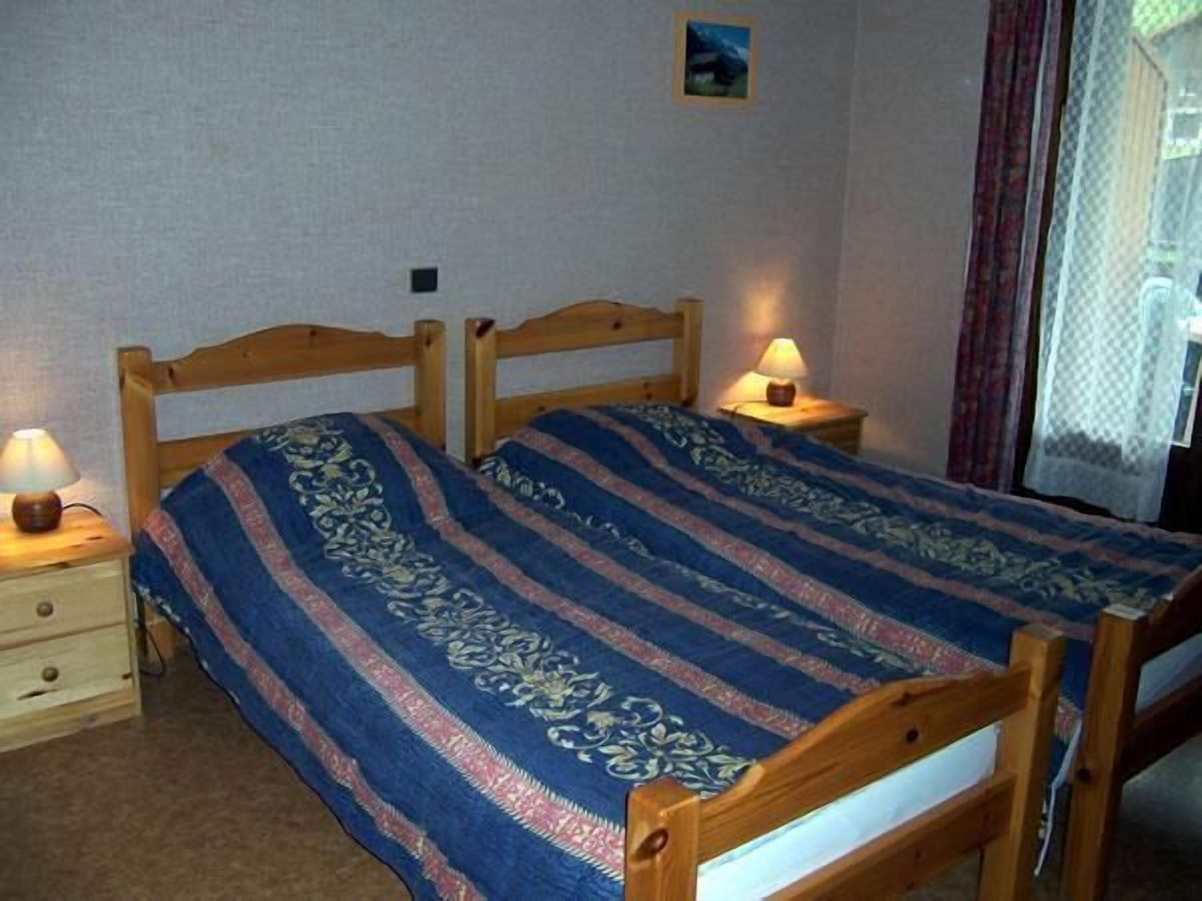 A bedroom with two wooden beds, each with a bedside table and lamp.
