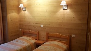 A room with two wooden beds, each with a headboard and a bedside table. There are wall-mounted lamps on either side of the beds. - 2nd floor, balcony, parking, ski locker, 51m², Le Grand Bornand (Le Grand-Bornand)