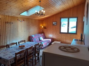 Ein gemütliches Blockhaus mit Esstisch, Stühlen, einer Couch und einer kleinen Küchenzeile.