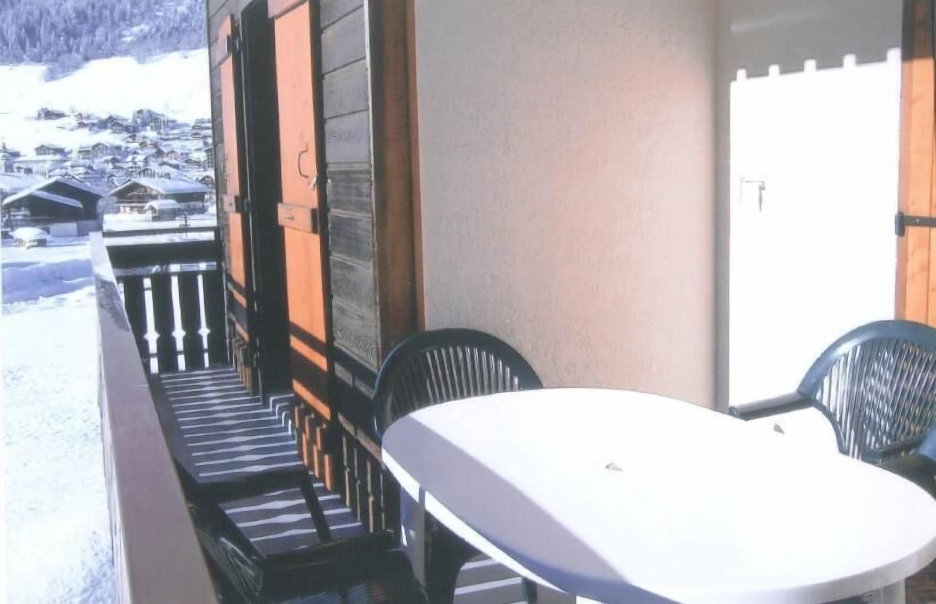 Un balcone con tavolo e sedie, affacciato su un villaggio innevato.