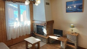 A cozy living room with a fireplace, a television, and a table. - 1st floor, balcony, fireplace or stove, parking, ski locker, 52m², Le Grand Bornand (Le Grand-Bornand)