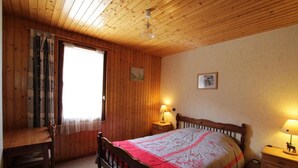 Een kamer met houten lambrisering, een bed, een tafel en twee bedlampjes.