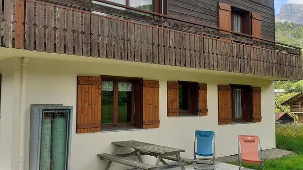 Een houten huis met twee verdiepingen, een balkon, een stenen terras en buiten zitplaatsen.