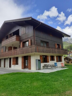 Ein zweistöckiges Gebäude mit einem Balkon im oberen Stockwerk, einer überdachten Außenlounge und Blick auf die Berge.