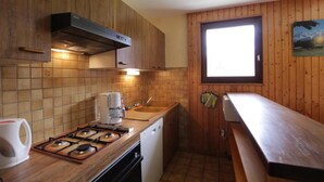 Een kleine keuken met houten kastjes, een gasfornuis, een koffiezetapparaat en een raam dat voor natuurlijk licht zorgt.
