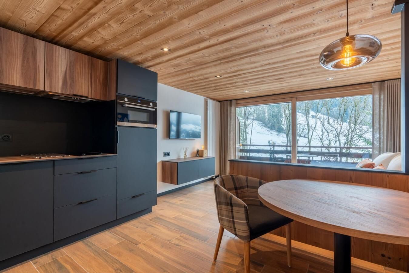 Eine moderne Küche mit dunklen Schränken, einer Holzbalkendecke und einem großen Fenster mit Blick auf eine verschneite Landschaft.