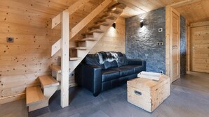 Un intérieur en bois avec un escalier, un canapé en cuir noir et un mur en pierre.