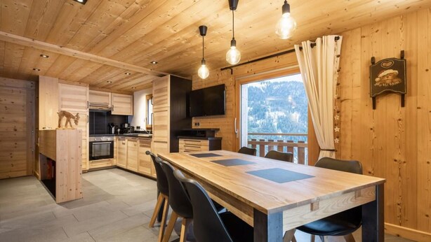 Un intérieur en bois comprenant un coin repas, une cuisine et une fenêtre donnant sur un paysage enneigé.