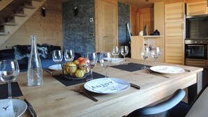 Une table de salle à manger en bois, mise avec des verres à vin, des assiettes et un panier de fruits.