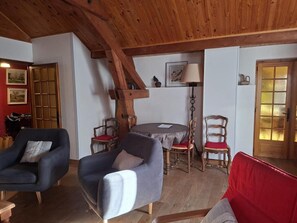 A cozy room with a wooden ceiling, a round table with chairs, and a red sofa. - Wifi, 3rd floor, view mountain, balcony, parking, tv, ski locker, 102m², Le Grand Bornand (Le Grand-Bornand)