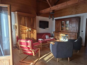 A wooden interior with a sofa, chairs, a television, and a bookshelf.