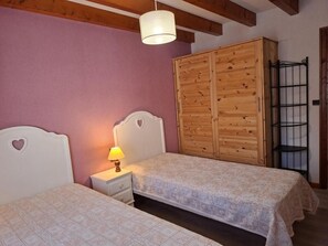 A bedroom with two beds, a wooden wardrobe, a nightstand with a lamp, and a metal shelf. - Wifi, 3rd floor, view mountain, balcony, parking, tv, ski locker, 102m², Le Grand Bornand (Le Grand-Bornand)