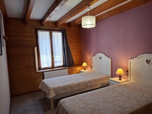 Een kamer met twee bedden, een raam met gordijnen, een radiator en een hanglamp.