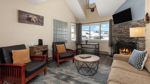 A cozy living room with a fireplace, comfortable seating, and a large window offering a view of the outdoors. - Wonderful 2 bedroom, pet friendly, ski-in/ski-out (Granby)