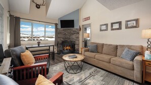 A living room with a stone fireplace, a sofa, a coffee table, and a television mounted on the wall. - Wonderful 2 bedroom, pet friendly, ski-in/ski-out (Granby)