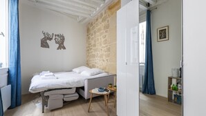 Une chambre à coucher avec un lit, une petite table, une armoire et un mur en pierre.