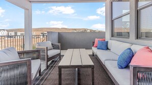 A covered outdoor seating area with a sofa, chairs, and a table, overlooking a desert landscape. - Azure Sands:  Desert Color Lagoon + Beaches + Hot Tub (St. George)