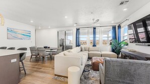 A modern living room with a sofa, chairs, a dining table, and a TV. - Azure Sands:  Desert Color Lagoon + Beaches + Hot Tub (St. George)