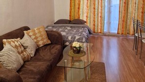 A living room with a brown sofa, patterned cushions, a glass coffee table, and a bed with a patterned bedspread. - Le Grand Robinson, 6 minutes from RER B Robinson, ideal for families. (Le Plessis-Robinson)