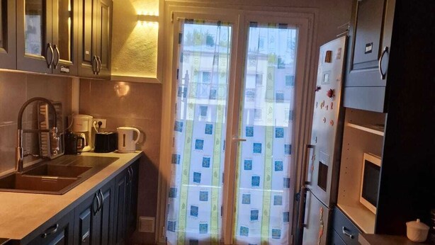 A compact kitchen with wooden flooring, dark cabinets, a built-in oven, and a window with patterned curtains. - Le Grand Robinson, 6 minutes from RER B Robinson, ideal for families. (Le Plessis-Robinson)