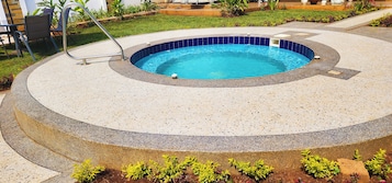 A circular swimming pool with a blue interior, surrounded by a pebble-patterned deck.