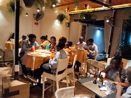 An outdoor dining area with round tables covered in orange tablecloths, surrounded by wicker chairs.