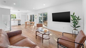 A modern living room with a brown leather sofa, a round coffee table, and a TV mounted on the wall. - Spacious, Bright Condo-Victoria Park Near Beach (Fort Lauderdale)