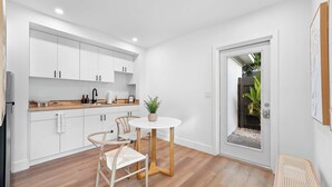 A modern kitchen with white cabinets, a wooden countertop, and a round table with chairs. - Modern Clean Studio Apartment Near Beach (Fort Lauderdale)