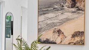 A dining area with a round table, a chair, a potted plant, and a framed coastal landscape painting on the wall. - Modern Clean Studio Apartment Near Beach (Fort Lauderdale)