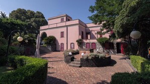 A building with a pink facade, a central courtyard with a staircase, and surrounding greenery. - LA GELSOMINA (Mascali)