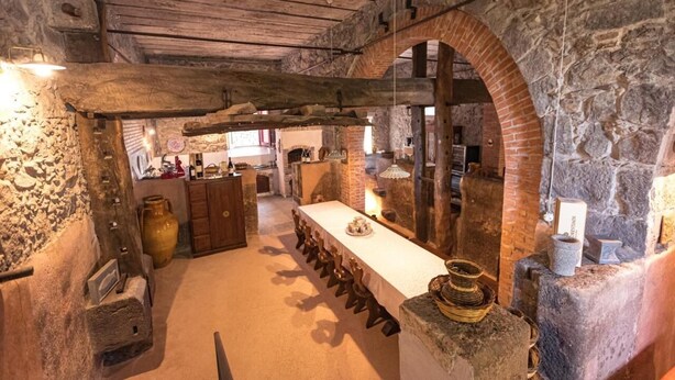 A rustic interior with stone walls, a long wooden table, and a brick archway. - LA GELSOMINA (Mascali)