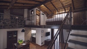 A spacious loft with exposed wooden beams, a loft bed, a dining area with a table and chairs, and a kitchen with a sink and countertop. - LA GELSOMINA (Mascali)
