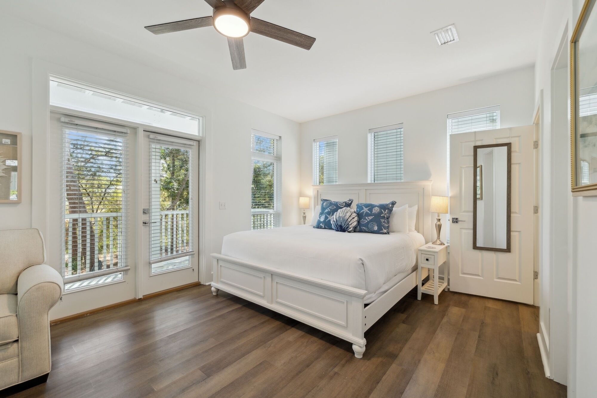 A bedroom with a large bed, a ceiling fan, and a view through the glass doors.