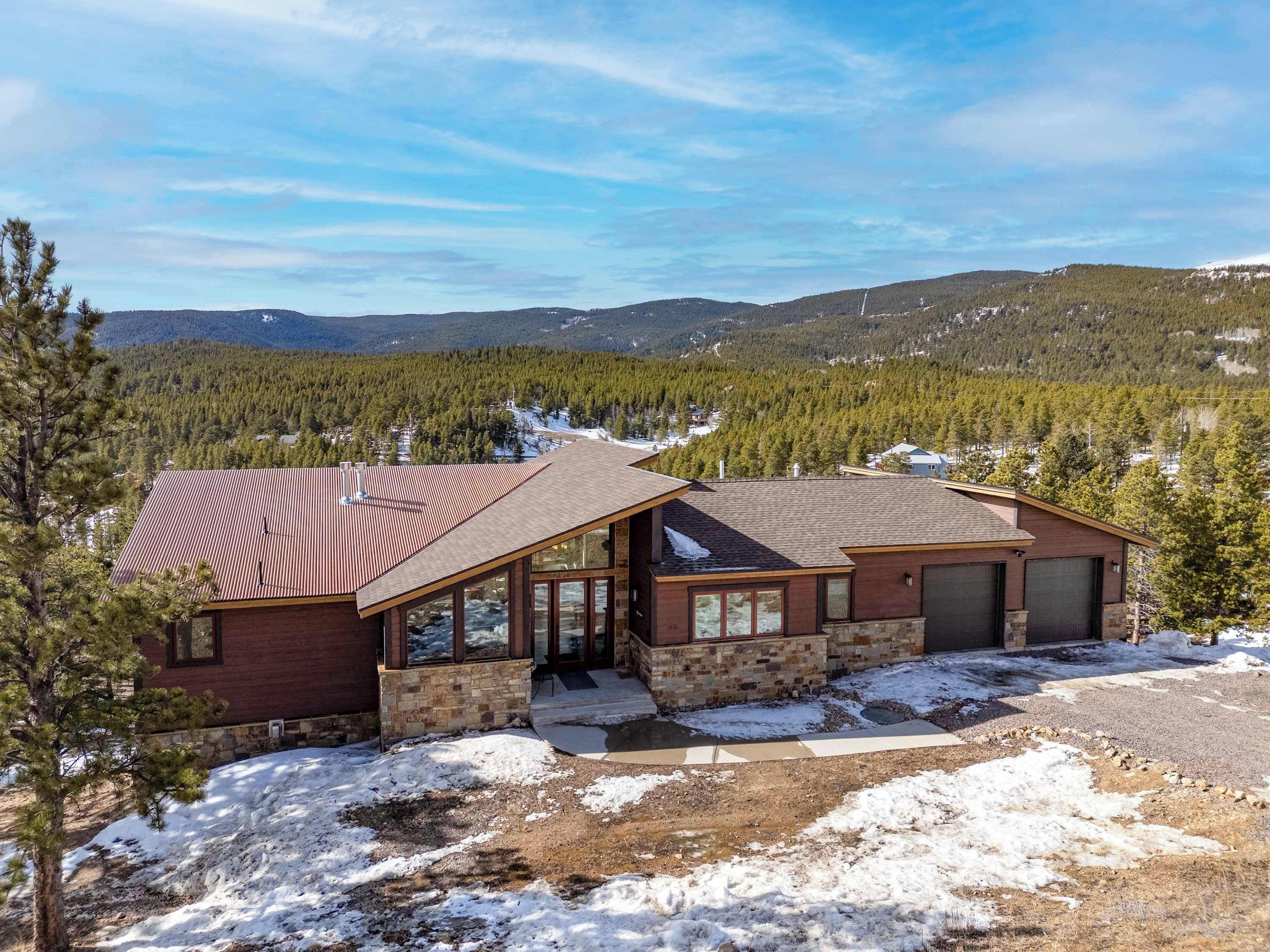 A two-story house with a stone foundation and a red roof, surrounded by a snowy landscape and dense forest.