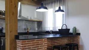 Una cocina con una isla de ladrillo, taburetes negros, luces colgantes y techo de madera.