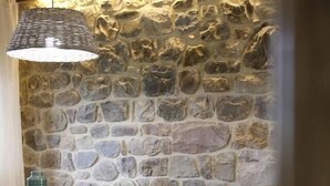 Un comedor con pared de piedra, mesa de madera, sillas negras y una lámpara colgante.