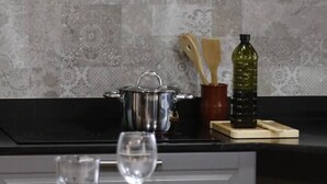 Una cocina con encimera negra, un plato blanco, una copa de vino, un vaso de agua, una olla, una botella y utensilios de madera.