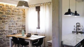 Un comedor rústico con pared de piedra, vigas de madera, una mesa con sillas e iluminación colgante.