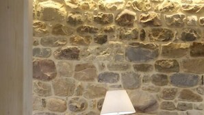 Una habitación con pared de piedra, un sofá blanco, una mesita de madera con una lámpara y un cuenco sobre la mesa.