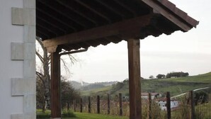 Un espacio al aire libre techado con pared de piedra, suelo de baldosas y vistas a un paisaje verde con colinas y una cerca.