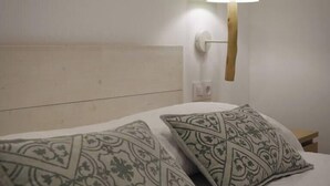 Una cama con almohadas estampadas y una lámpara fijada a la pared.