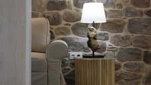 A room with a stone wall, a round wooden side table with a lamp, and a beige sofa.