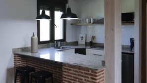 A modern kitchen with a brick accent wall, a large island with bar stools, pendant lighting, and a view of the dining area.