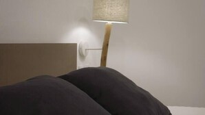 A bed with two dark pillows and a wall-mounted lamp.