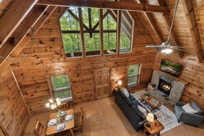 L’intérieur d’une cabane en rondins comprend un coin repas, un canapé, une cheminée et de grandes fenêtres.