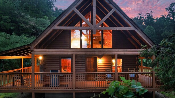 A wooden cabin with a balcony and large windows, surrounded by forest. - Top Location!Easy Drive-Hot Tub-Fire Pit-Games (Pigeon Forge)