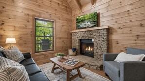 A cozy cabin interior with a stone fireplace, wooden walls, a sofa, and a television. - Top Location!Easy Drive-Hot Tub-Fire Pit-Games (Pigeon Forge)