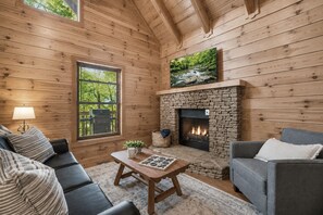A cozy cabin interior with a stone fireplace, wooden walls, a sofa, and a television.