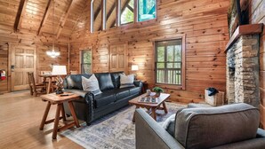 A cozy log cabin interior with a black leather sofa, a wooden coffee table, and a stone fireplace. - Top Location!Easy Drive-Hot Tub-Fire Pit-Games (Pigeon Forge)