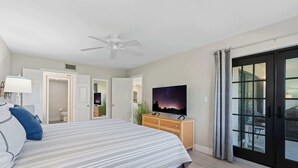 A bedroom with a bed, a TV, a ceiling fan, and a sliding glass door to the outside. - F-338 -Beautiful Resort and Sunset Views! (Naples)